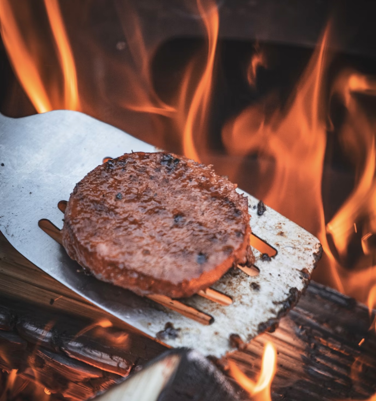 焼き網の上で炎をあげて焼かれる分厚いハンバーグステーキ
