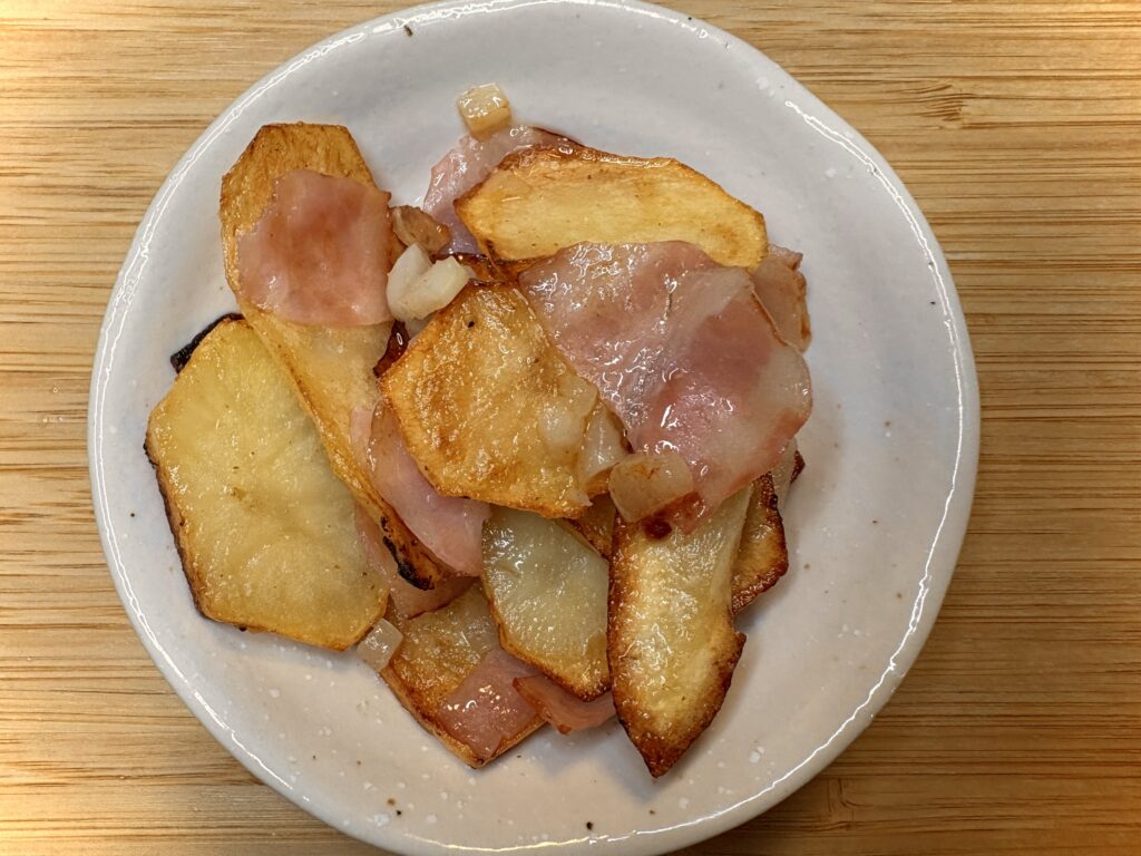 薄切りポテトとベーコンをこんがり焼き上げたジャーマンポテト。白い皿に盛り付けられている。