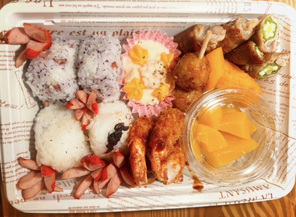 行事の日のお弁当。ゆかりおにぎりと白ごまおにぎり、タコさんウインナー、卵焼き、肉巻きオクラ、唐揚げ、エビフライ、デザートの黄桃。