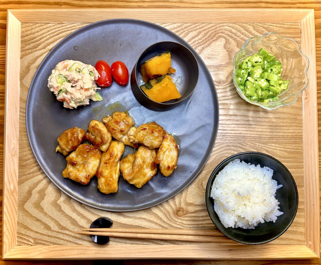 鶏のハニーマスタード焼き、ポテトサラダ、かぼちゃの煮物、刻んだオクラ、副菜と白ごはんを木のトレイに盛り付けた和風の晩ごはん