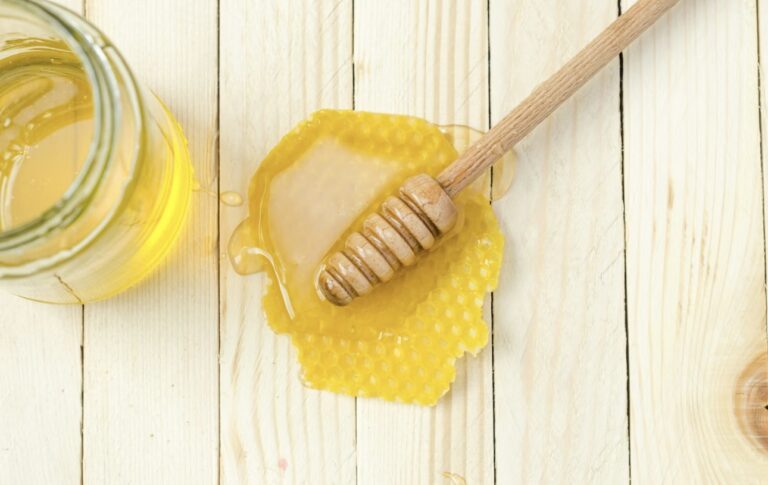 「木のスプーンに絡めたはちみつと、ガラス瓶、木のテーブルに広がるハチの巣の蜜蝋」