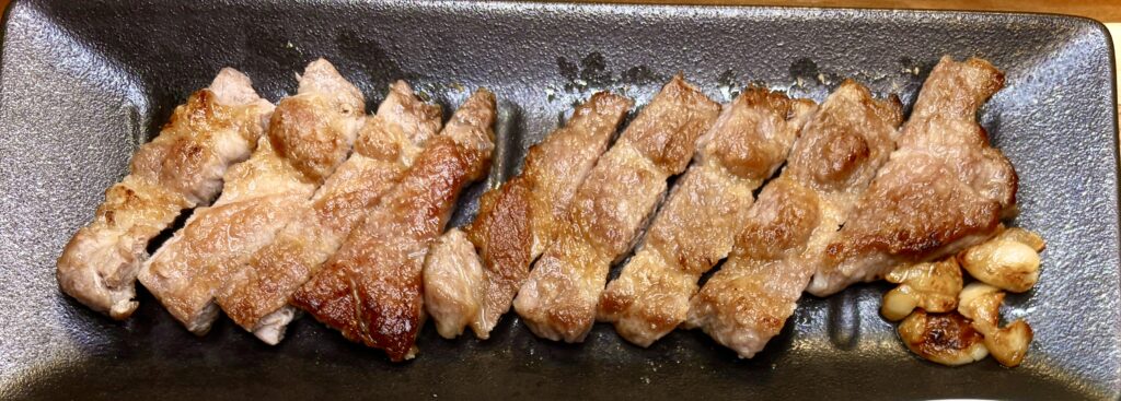 にんにく風味のポークソテー。香ばしく焼き上げた豚肉が食べやすくカットされ、付け合わせに焼きにんにくが添えられている