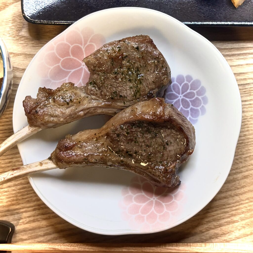 白い花柄の皿に盛られた骨付きラムチョップ2本。表面にはこんがりとした焼き色が付き、脂がつややかに光っている。ジューシーで香ばしい香りが伝わってくるようなメインディッシュの一皿。