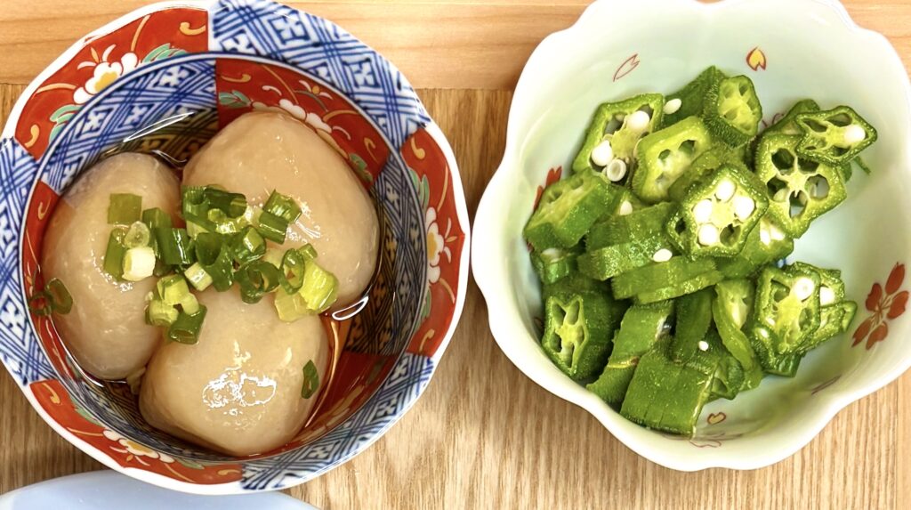 和柄の器に盛られた玉こんにゃくの煮物(刻みネギのせ)と、白い器に入った小口切りのオクラのおひたし