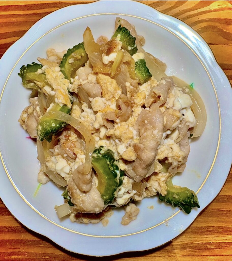 白い皿に盛られたゴーヤチャンプルー。豚肉、玉ねぎ、豆腐、卵が炒め合わされ、ゴーヤの緑がアクセントになった彩り豊かな沖縄風炒め料理。