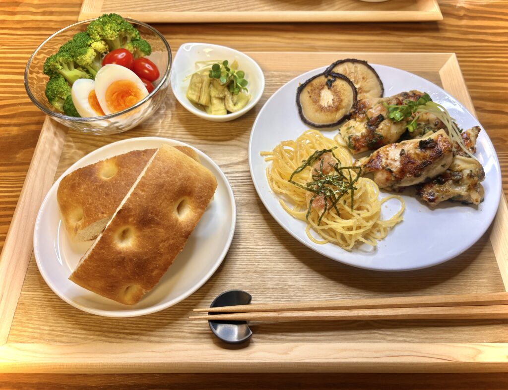 鶏肉のグリルと明太子パスタ、フォカッチャ、ゆで卵入りサラダが並ぶ彩り豊かな夕食プレート