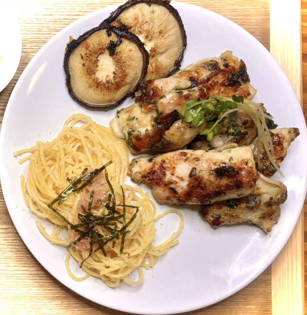 ジューシーに焼き上げた鶏肉のグリルと椎茸ソテー、明太子パスタが盛り付けられた白い皿