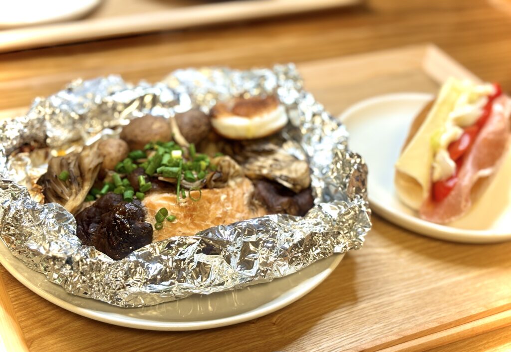 秋鮭ときのこのホイル焼きと、生ハムとチーズのサンドイッチの食卓。アルミホイルを開けた瞬間、鮭ときのこの香りが広がる一皿と、彩り豊かなサンドイッチが並んでいる。