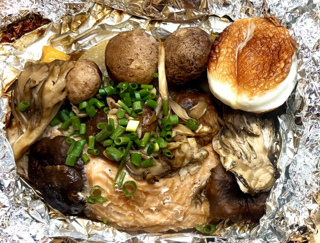 アルミホイルの中で焼き上げた秋鮭と、椎茸・マッシュルーム・舞茸・玉ねぎ・パプリカなどの野菜。上には刻みねぎが散らされ、香ばしく焼けたきのこと鮭の旨みがぎゅっと詰まったホイル焼き。
