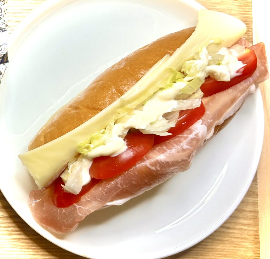 白い皿にのせられたサンドイッチ。生ハム、トマト、レタス、チーズ、マヨネーズをふんわり挟んだ彩り豊かな一品。