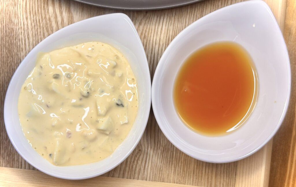 木目のトレーに置かれた白い小鉢2つ。左の小鉢には手作りのタルタルソースがたっぷり入り、右の小鉢には透き通った琥珀色の甘酢が注がれている。