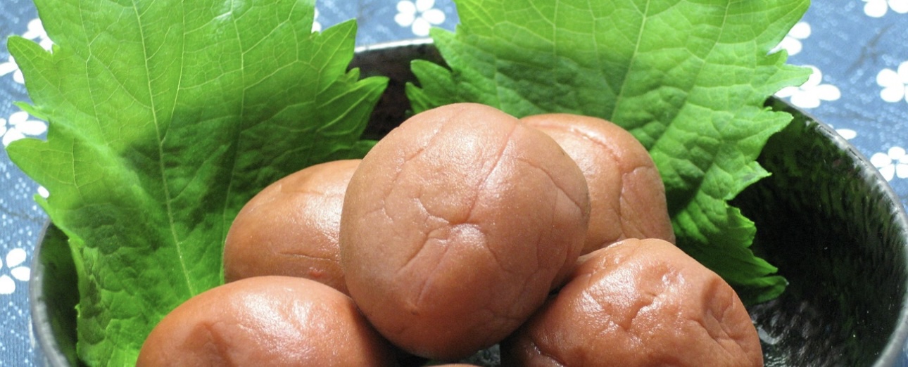 黒い器に盛られた梅干しと青じその葉。鮮やかな緑のしそと、つやのある赤茶色の梅干しが和風の雰囲気を演出している