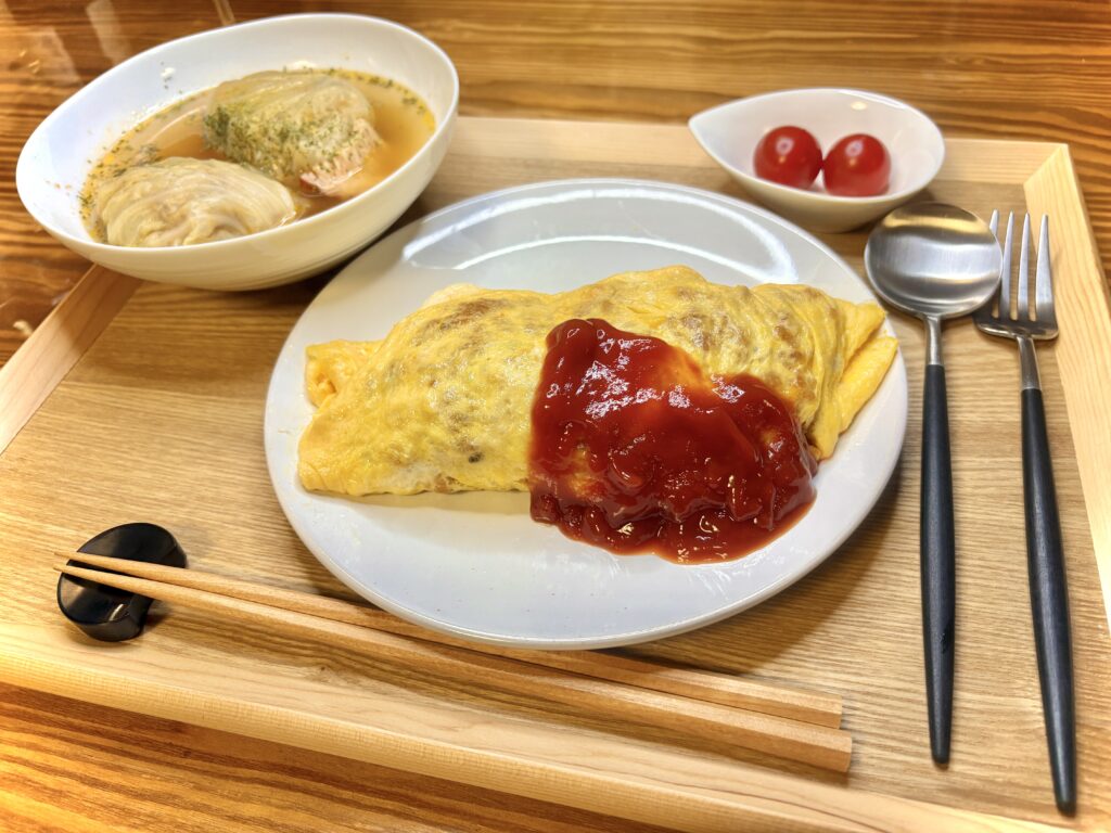 「木のトレーに盛り付けられた晩ごはん。ケチャップをかけたふんわり卵のオムライス、スープで煮込んだロールキャベツ2つ、付け合わせのプチトマトが並んでいる」
