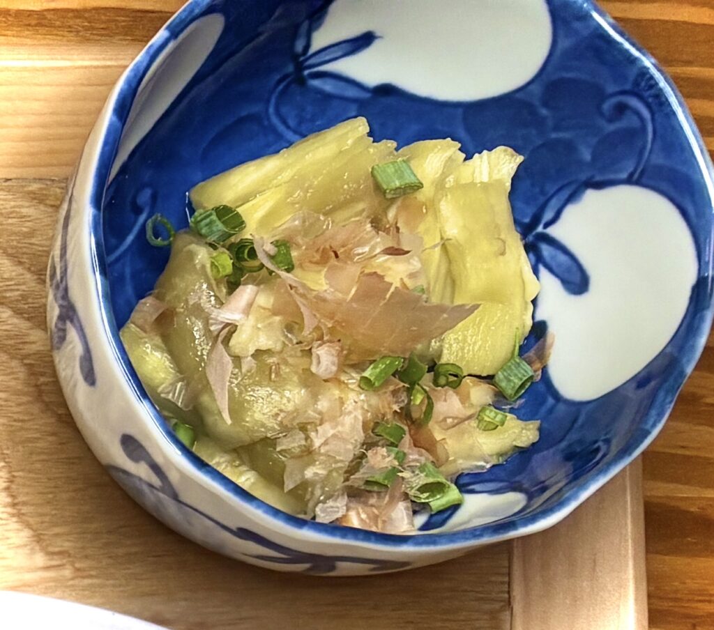 青と白の器に盛られた焼きなす。鰹節と刻みねぎがトッピングされ、出汁の風味が感じられる和風の副菜。
