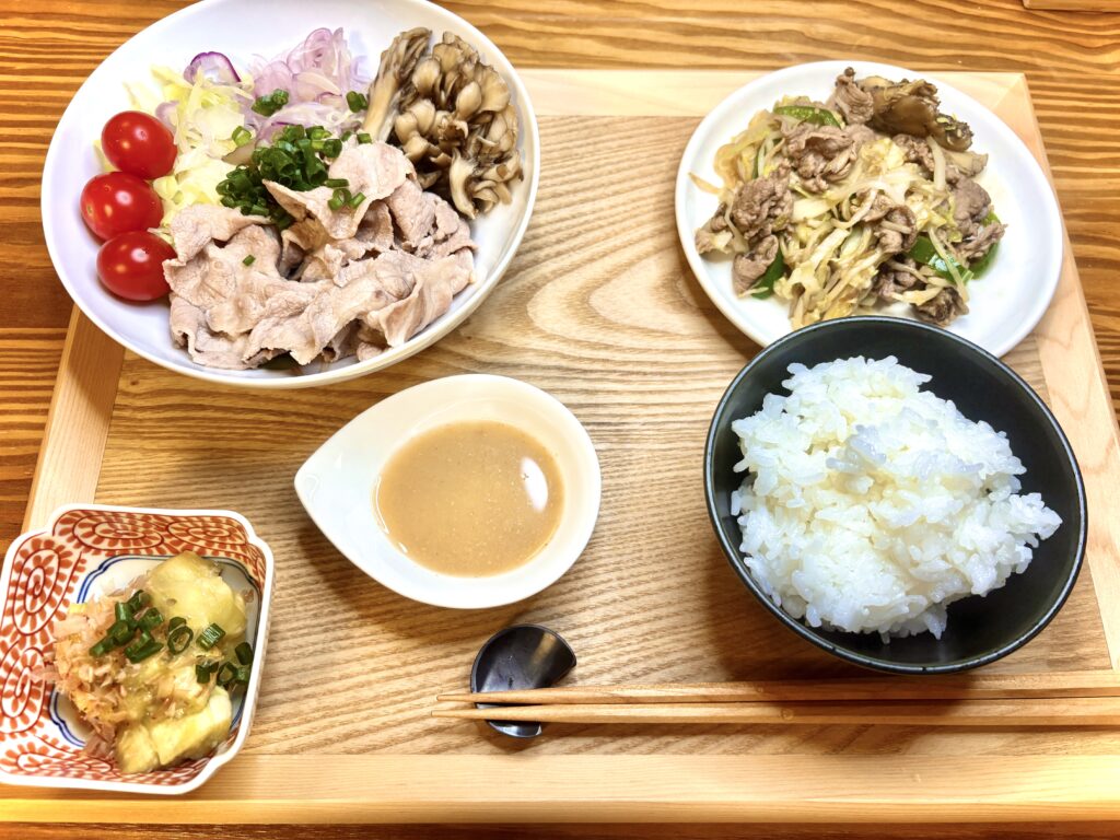 「豚しゃぶサラダにトマトと舞茸を添え、ゴマだれで味わう和定食。ごはん、ジンギスカン炒め、焼きなす小鉢が並ぶ一汁三菜スタイル」