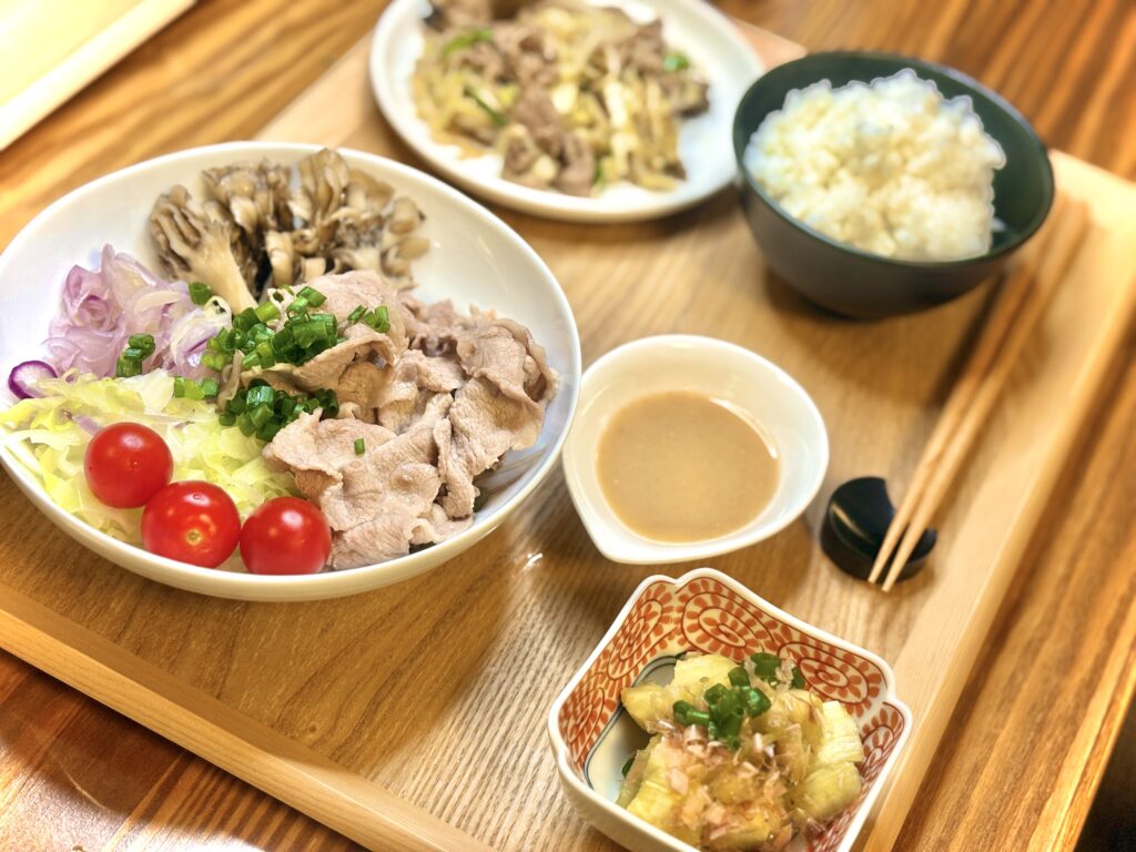 彩り豊かな冷しゃぶサラダ、焼きなすの小鉢、ジンギスカン炒めと白ごはんを木のトレーに盛り付けた献立