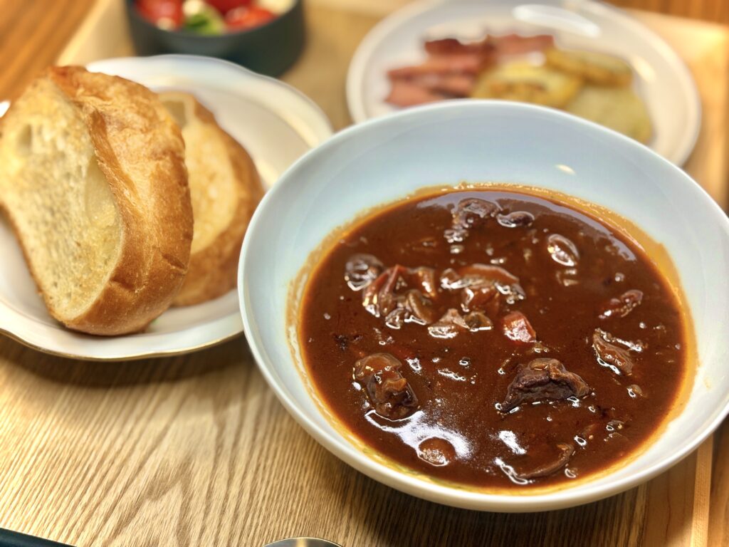 白い器に盛られた濃厚なビーフシチュー。大きめにカットされた牛肉や野菜がたっぷり入り、照りのあるソースが食欲をそそる。隣にはこんがり焼き色のついた厚切りバゲットが添えられ、シチューと一緒に楽しめる洋食セット。