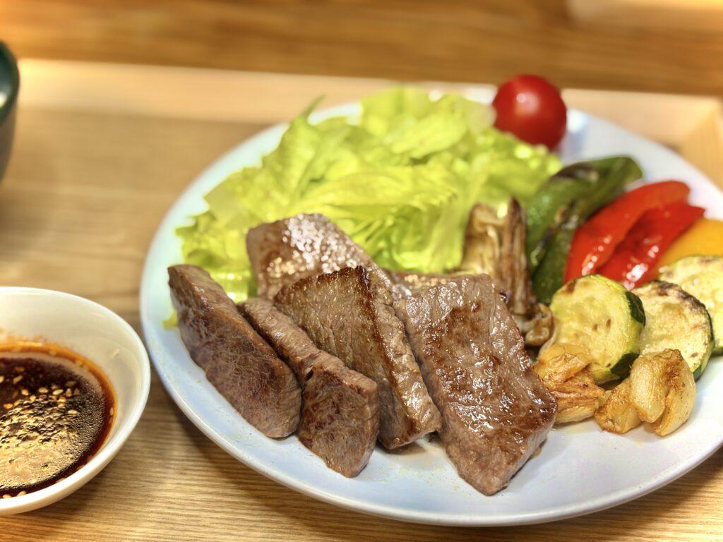厚切りに焼いたジューシーなステーキと彩り豊かな野菜、レタスやパプリカ、ズッキーニが盛られたプレート。横にはごま入りの焼肉のタレが添えられている