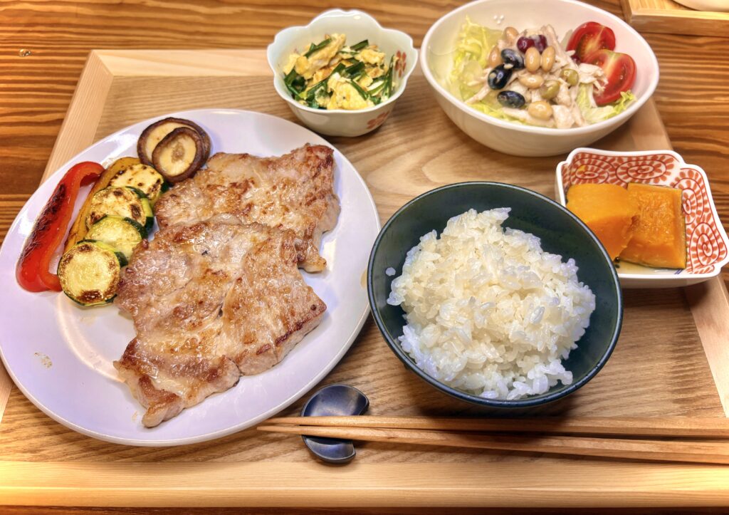 ジューシーに焼き上げたトンテキとグリル野菜、ニラ玉、かぼちゃの煮物、豆サラダ、白ごはんをそろえた栄養バランスの良い晩ごはん定食
