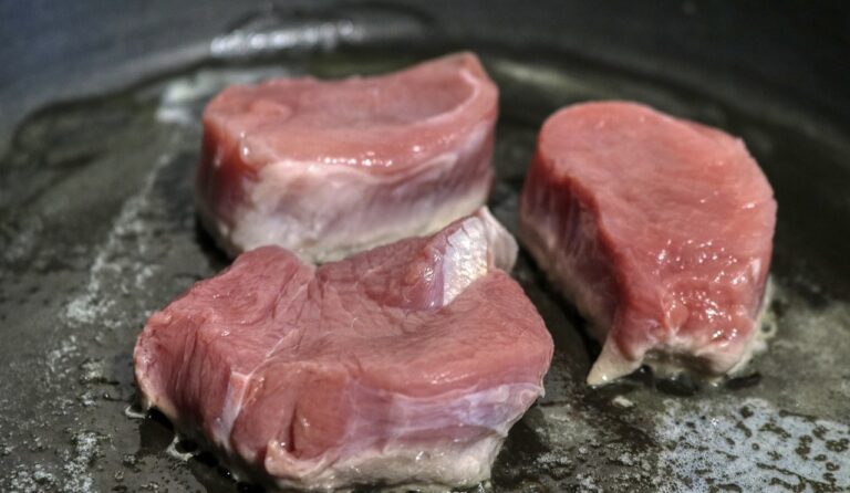 フライパンで焼き始めた分厚い豚肉。ジューシーなトンテキ用にこんがりと焼き色をつけている調理中の様子