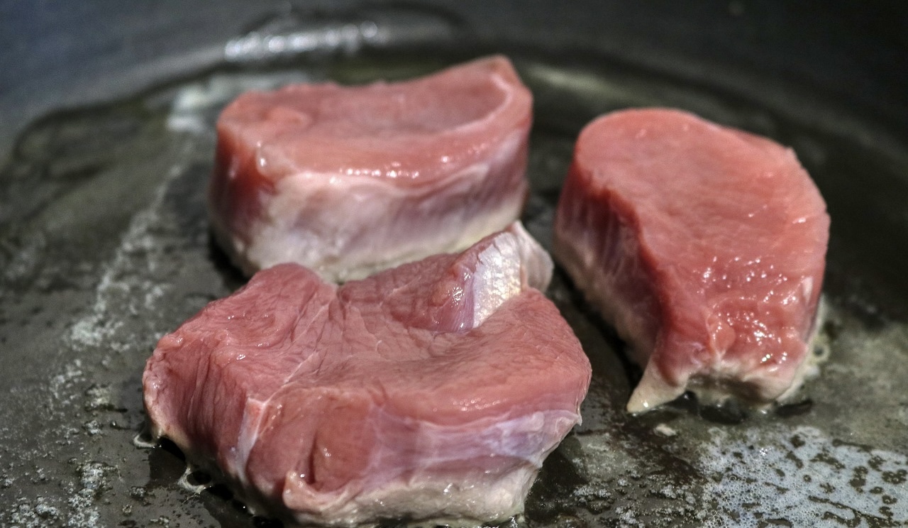 フライパンで焼き始めた分厚い豚肉。ジューシーなトンテキ用にこんがりと焼き色をつけている調理中の様子
