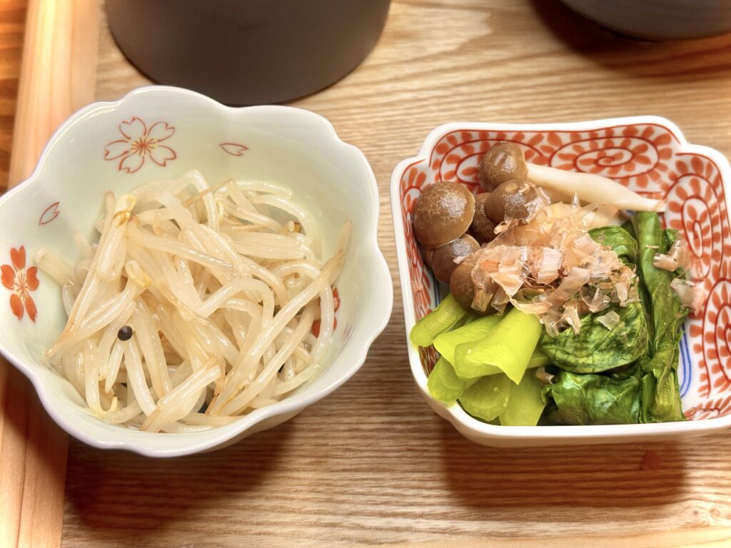 桜柄の器にもやしナムル、赤い模様の器に小松菜としめじのおひたし。鰹節がのって、彩りも風味も豊かな和風の小鉢料理。