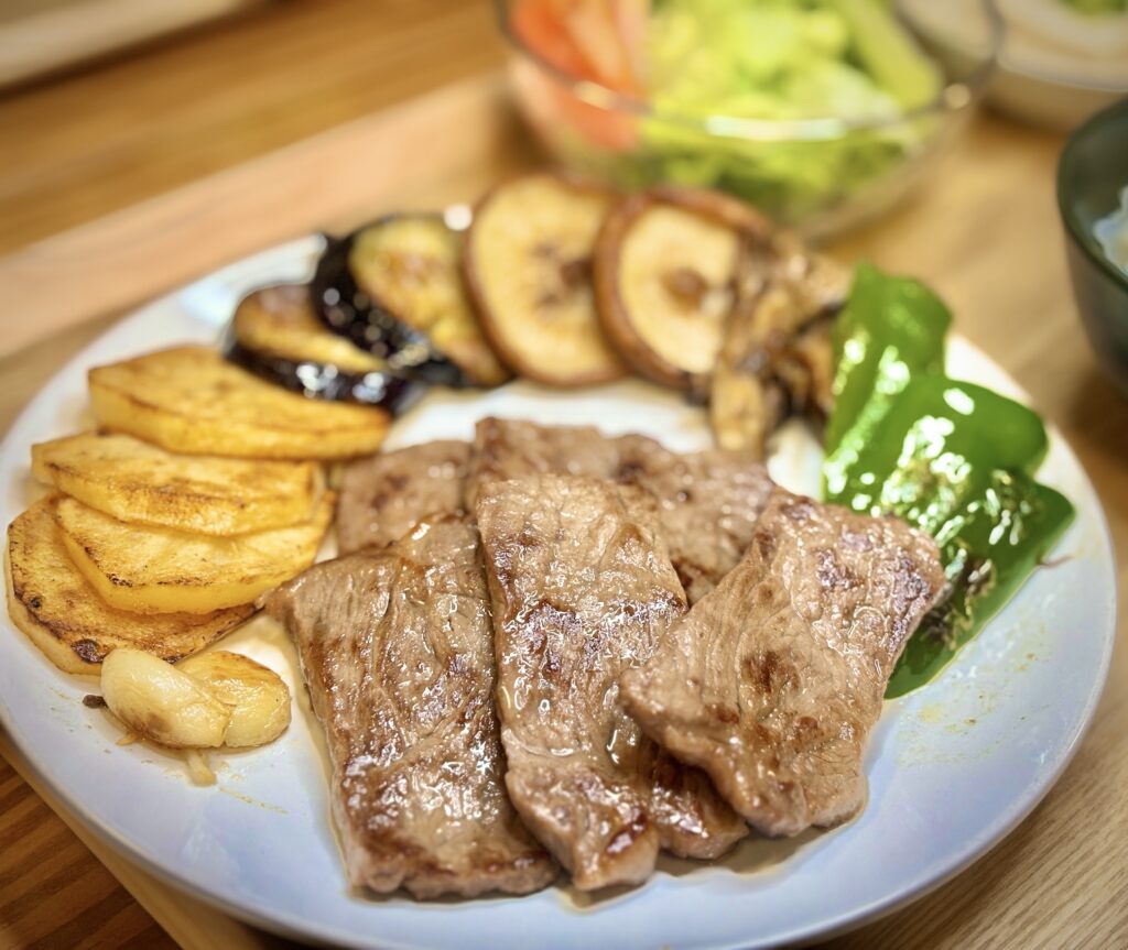 白い皿に盛られた焼肉プレート。ジューシーな牛肉の横には、こんがり焼いたポテト、香ばしいにんにく、しいたけやなす、ピーマンなどの野菜が並び、彩り豊かな一皿。