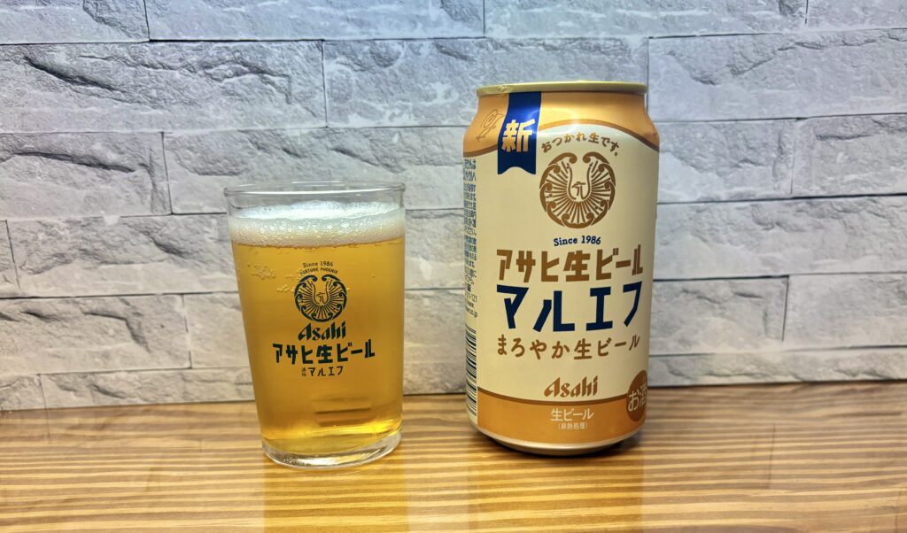 木目のテーブルの上に、アサヒ生ビール「マルエフ」の缶とグラスが並んでいる写真。
グラスには淡い黄金色のビールが注がれ、きめ細かな泡がうっすらと残っている。
背景は白いレンガ調の壁で、落ち着いた雰囲気の中にまろやかな生ビールの魅力が伝わる構図。