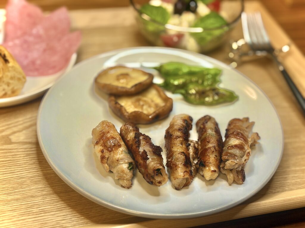 白いプレートに盛り付けられた豚肉の紫蘇巻き4本と、椎茸、ししとうのソテー