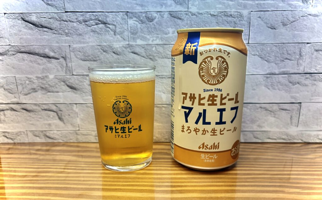 木目のテーブルの上に、アサヒ生ビール「マルエフ」の缶とグラスが並んでいる写真。
グラスには淡い黄金色のビールが注がれ、きめ細かな泡がうっすらと残っている。
背景は白いレンガ調の壁で、落ち着いた雰囲気の中にまろやかな生ビールの魅力が伝わる構図。