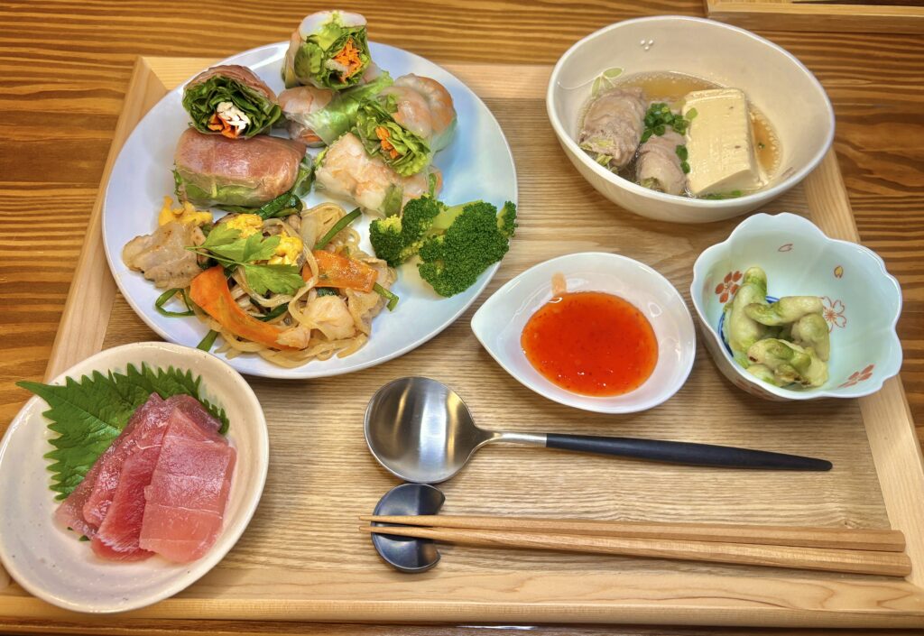 エビと鶏むね肉・アボカドの生春巻き、チーズ生ハムの生春巻き、パッタイ、柚豆腐の出汁煮、枝豆の天ぷら、まぐろの刺身を盛り合わせた和×アジアンの晩ごはんプレート。木のトレイに整然と並び、彩り豊かでカフェ風の食卓。
