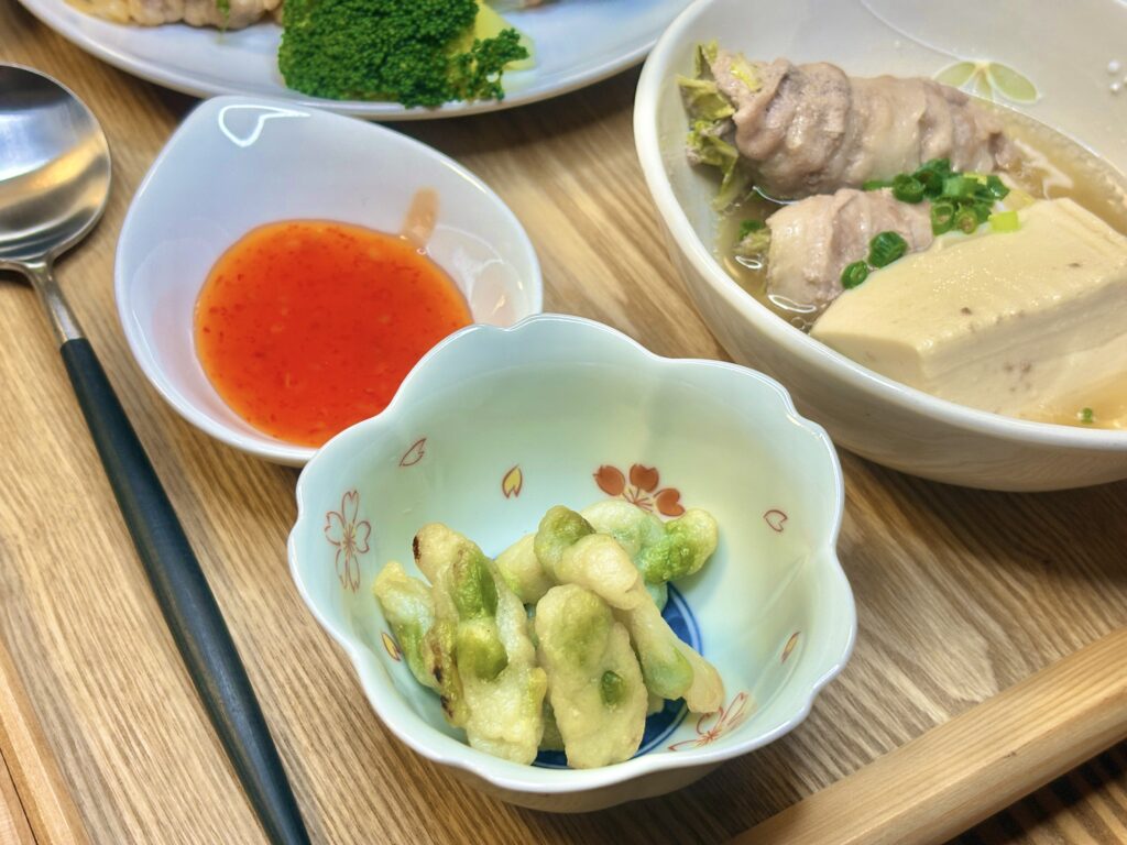 枝豆の天ぷら、スイートチリソース、柚豆腐と白菜の豚肉巻きの出汁煮を木のトレイに並べた和風アジアンな一皿。やさしい色合いの器が料理の彩りを引き立て、家庭的で落ち着いた雰囲気の食卓。