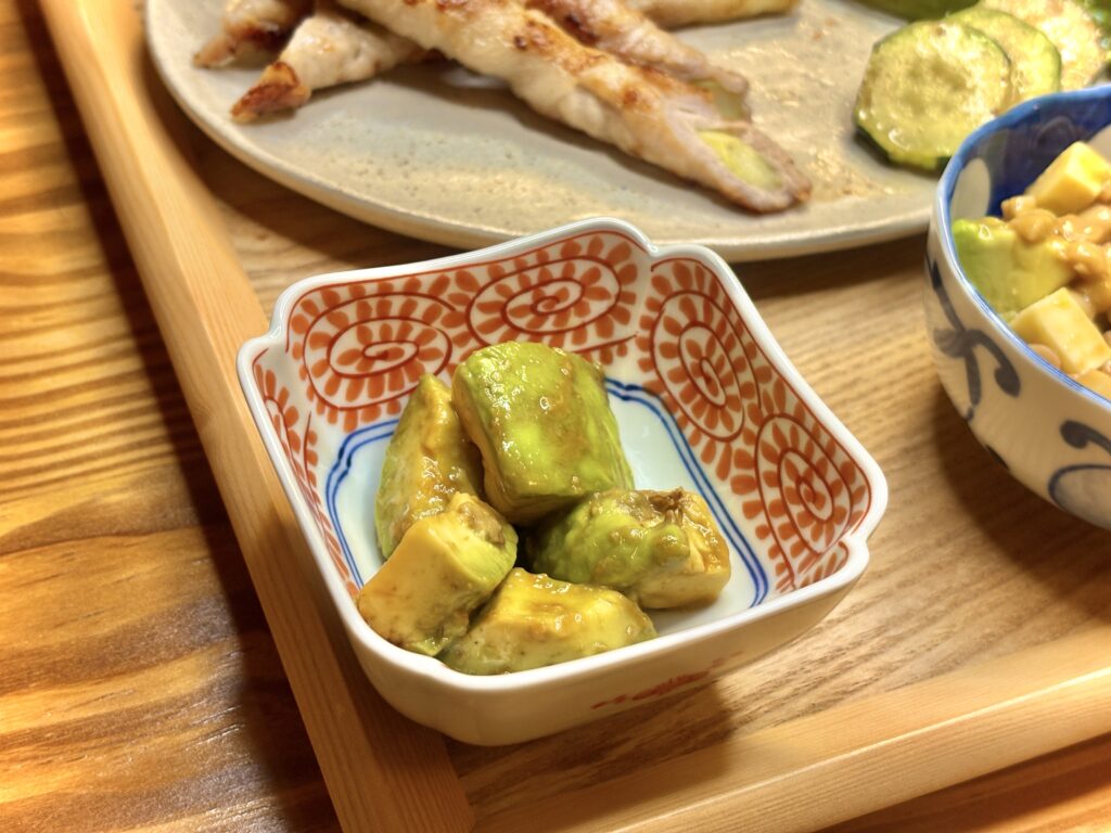 角皿に盛り付けたアボカドのわさびあえ。つややかな緑色が映える副菜で、木のトレーの上に並ぶ家庭の一品料理。