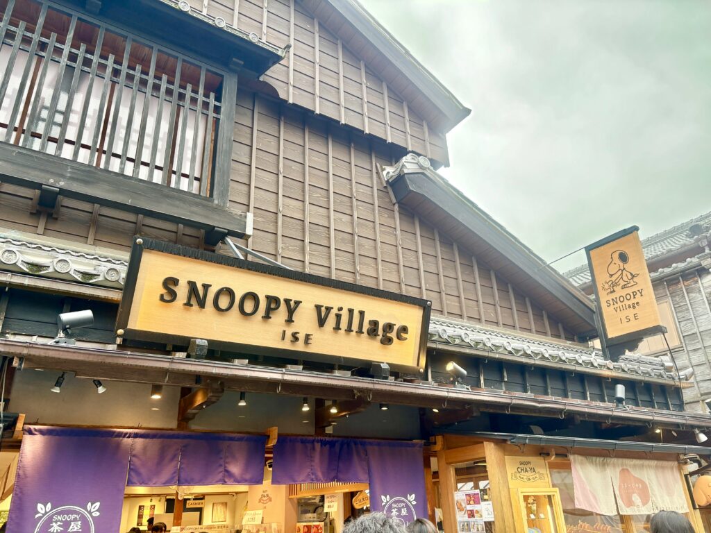 おかげ横丁にある「スヌーピービレッジ伊勢」の外観。木の看板と紫ののれんが印象的で、町屋造りの建物にスヌーピーのロゴがかわいく映える。観光客でにぎわう人気スポット。