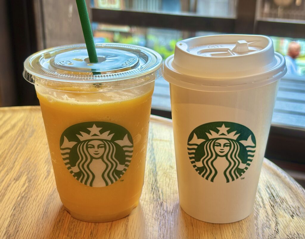 伊勢おかげ横丁のスターバックスで注文したドリンク。木のテーブルに置かれたホットコーヒーとマンゴーフラペチーノが、和風の窓辺の景色と調和している様子。