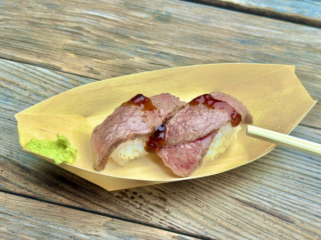 伊勢おかげ横丁で味わえる松阪牛のにぎり寿司。香ばしく炙られたお肉がシャリにのり、上には甘辛いタレがとろり。横にはわさびが添えられ、贅沢な味わいを予感させる一皿。