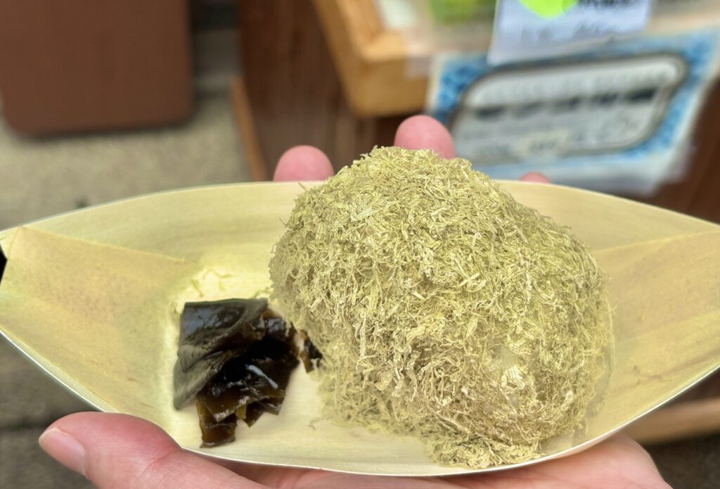 伊勢おかげ横丁で販売されている「とろろ昆布おにぎり」。ふんわりとしたとろろ昆布がたっぷりと巻かれ、横にはつややかな昆布の佃煮が添えられている。素朴で優しい味わいが人気の一品。