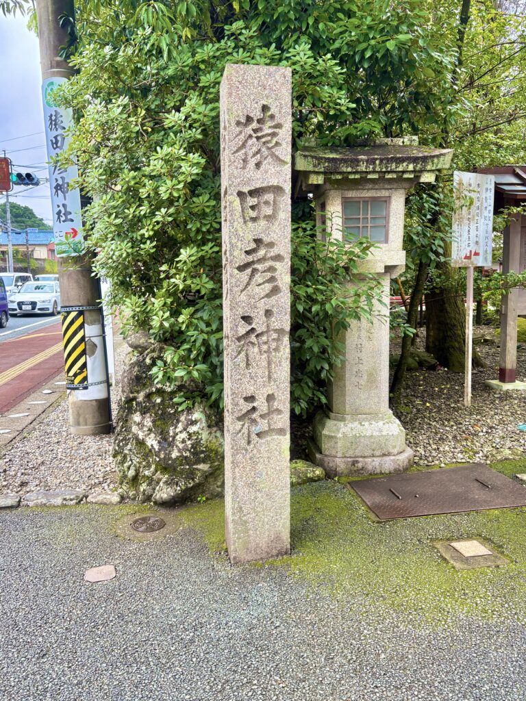 三重県伊勢市にある猿田彦神社の石碑。緑に囲まれた参道入口に立つ「猿田彦神社」と刻まれた石柱が、歴史と厳かな雰囲気を感じさせる。旅の安全や導きの神として知られる神社の入り口風景。