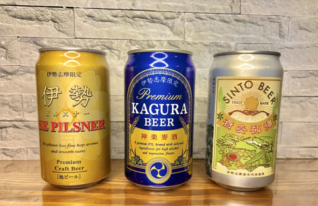 伊勢志摩限定クラフトビール3種類が並んでいる写真。
左から「伊勢ピルスナー(黄金色)」「神楽麦酒(深い青)」「神都麦酒(クリーム色)」の3本。
それぞれ異なるデザインの缶が並び、個性豊かな色合いが映える。