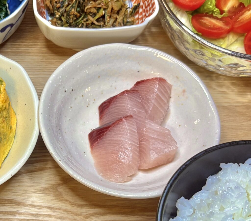 脂ののった鰤の刺身が3切れ並ぶ小皿。ピンクがかった身の美しいグラデーションが新鮮さを感じさせ、シンプルながら存在感のある一品。
