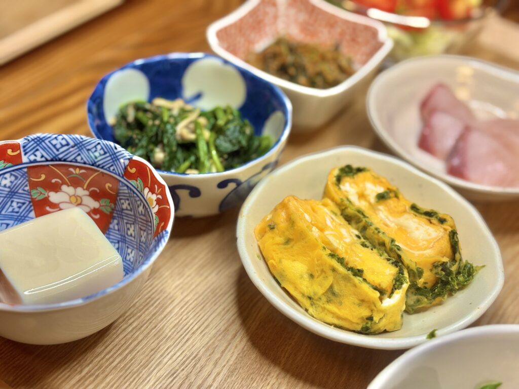 青さ入りのだし巻き卵がふっくらと盛られた小皿。隣には冷奴やほうれん草のナムル、小鉢のおかずが並び、彩り豊かな和食の一角を演出している。