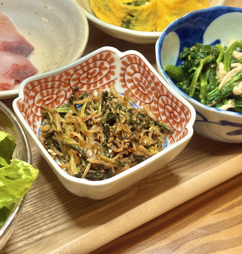 大根葉としらすを香ばしく炒めた副菜。ごま油の香りが立ち、白ごまがアクセントになった彩り豊かな一品。小ぶりの和柄の器に盛り付けられている。