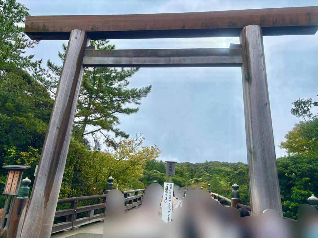 伊勢神宮・内宮の宇治橋に立つ大鳥居。木のぬくもりを感じる鳥居の向こうに、参拝客が行き交う神聖な参道と豊かな緑が広がっている様子。