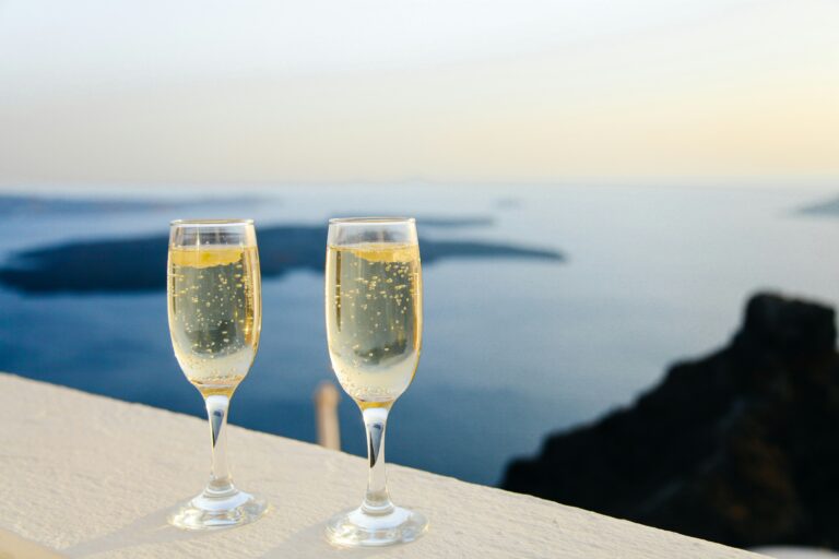 夕暮れの海を背景に、シャンパングラスで乾杯する2杯のスパークリングワイン。旅の夜の穏やかなひととき。