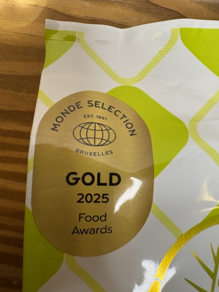 「モンドセレクション2025金賞」のゴールドラベル部分をアップで撮影した写真。
光沢のある金色のマークに「GOLD 2025 Food Awards」と記載されており、
伊勢ねぎらいねぎ天ぷらえびせんべいの高評価を示す受賞シールが輝いている。