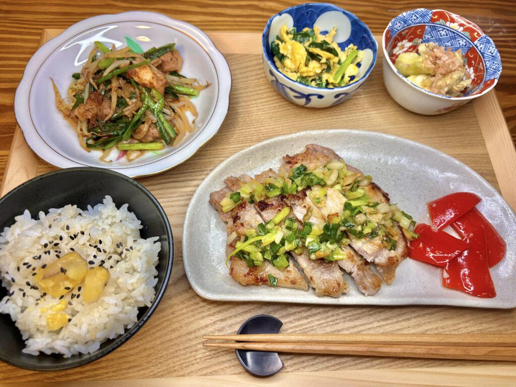 木のトレーに並べられた秋の和定食。メインのポークソテーねぎにんにくごま油ソース、三重名物の亀山ホルモン炒め、にら玉、焼きなす、もち米入りの栗ごはんが彩りよく並ぶ。