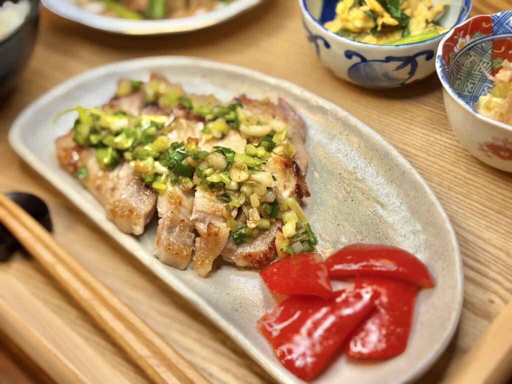 香ばしく焼き上げたポークソテーに、ねぎとにんにくのごま油ソースをたっぷりかけた一皿。横には鮮やかな赤パプリカが添えられ、彩り豊かな秋のメイン料理。」