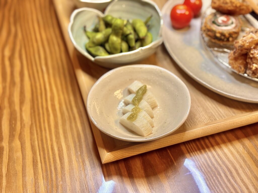 白い小皿に盛られたかまぼこに、わさびが添えられている。木のテーブルの上に置かれた前菜の一品