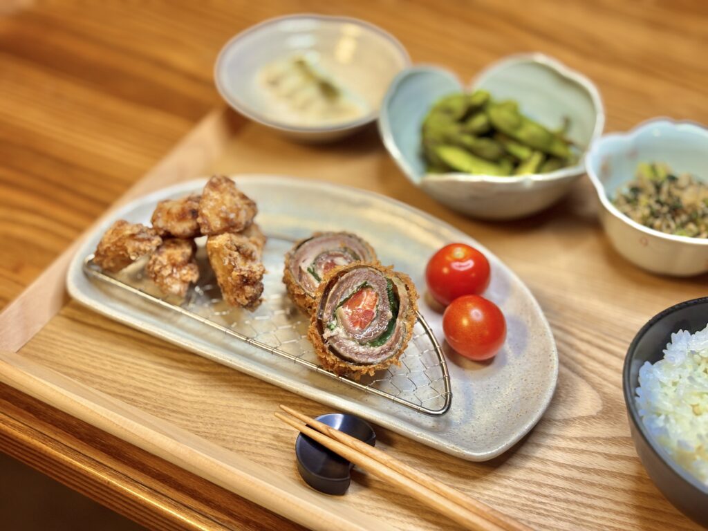 秋刀魚の紫蘇チーズトマト巻きと里芋の唐揚げを盛り付けたプレート。金網の上に並べられ、横にはミニトマトが添えられている。」
