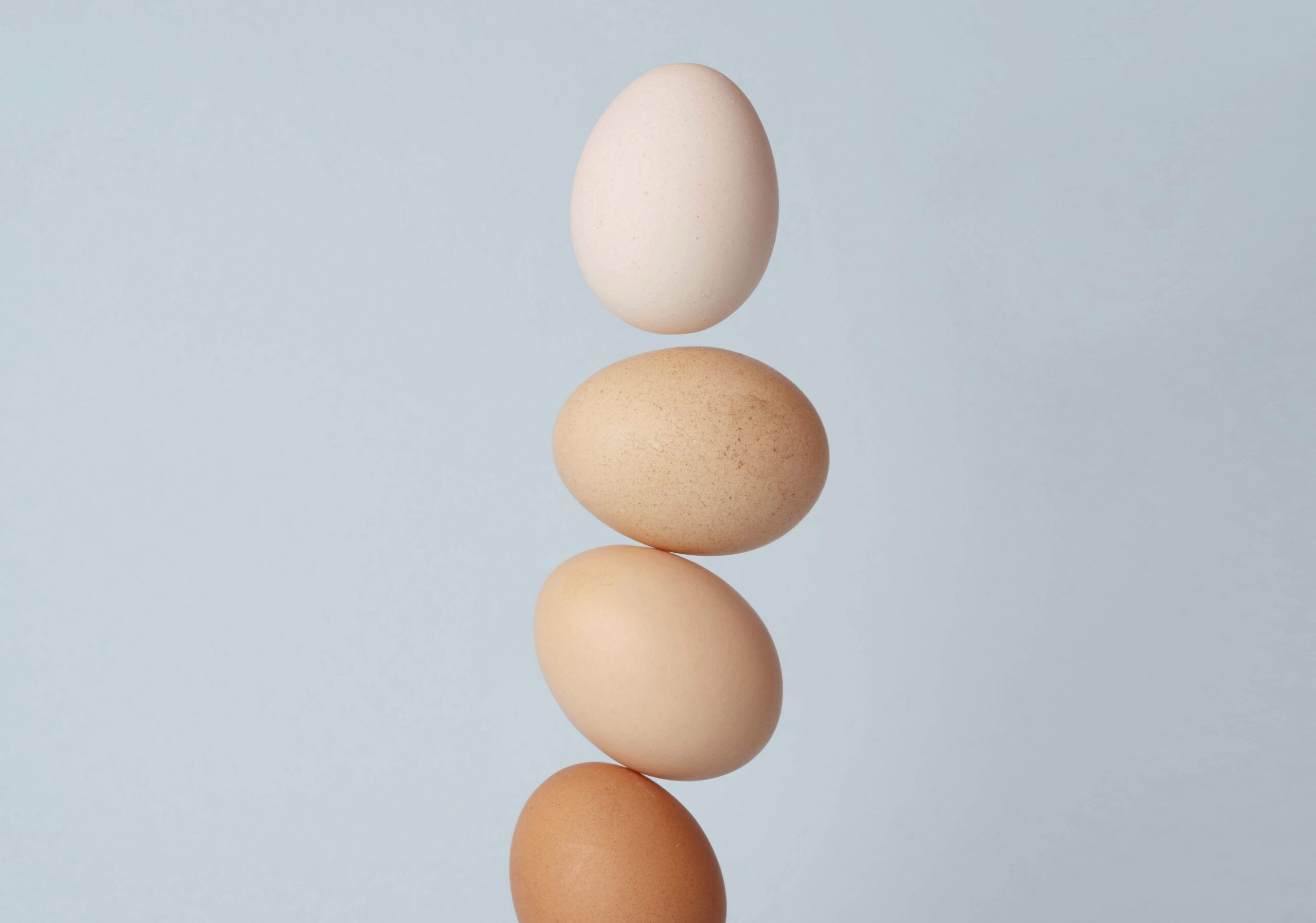 淡いブルーの背景に、4つの卵が縦にバランスよく積み重なっている。上から順に色味が異なり、白から茶色までのグラデーションが美しい。